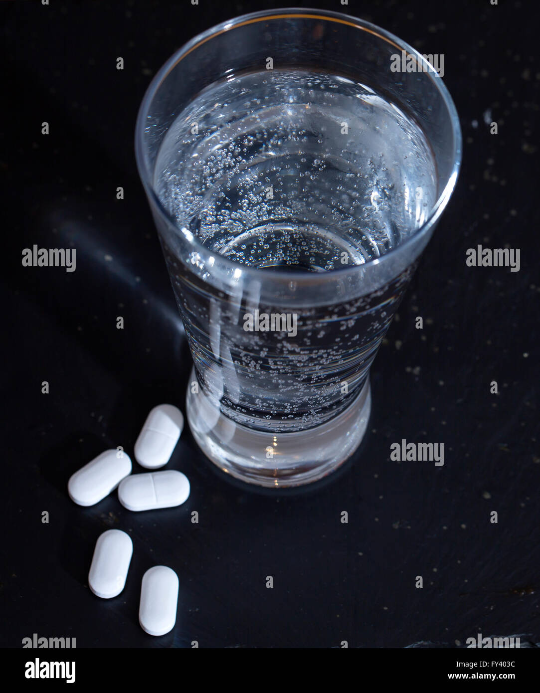 Morgen nach der Nacht zuvor. Ein Stillleben Bild von Mineralwasser mit einigen Vitamintabletten mit einem dunklen Hintergrund. Stockfoto