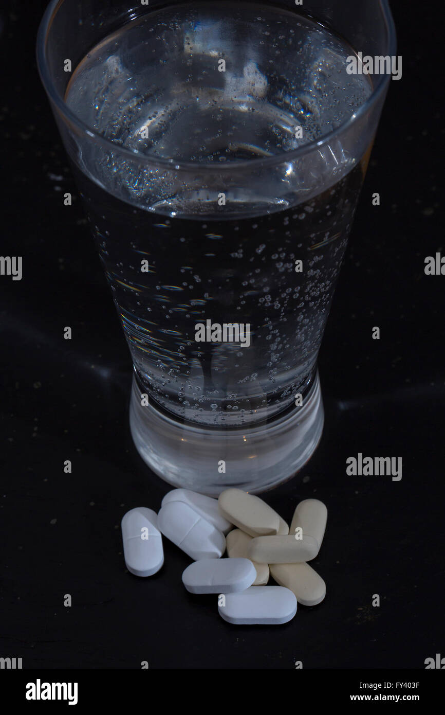 Morgen nach der Nacht zuvor. Ein Stillleben Bild von Mineralwasser mit einigen Vitamintabletten mit einem dunklen Hintergrund. Stockfoto