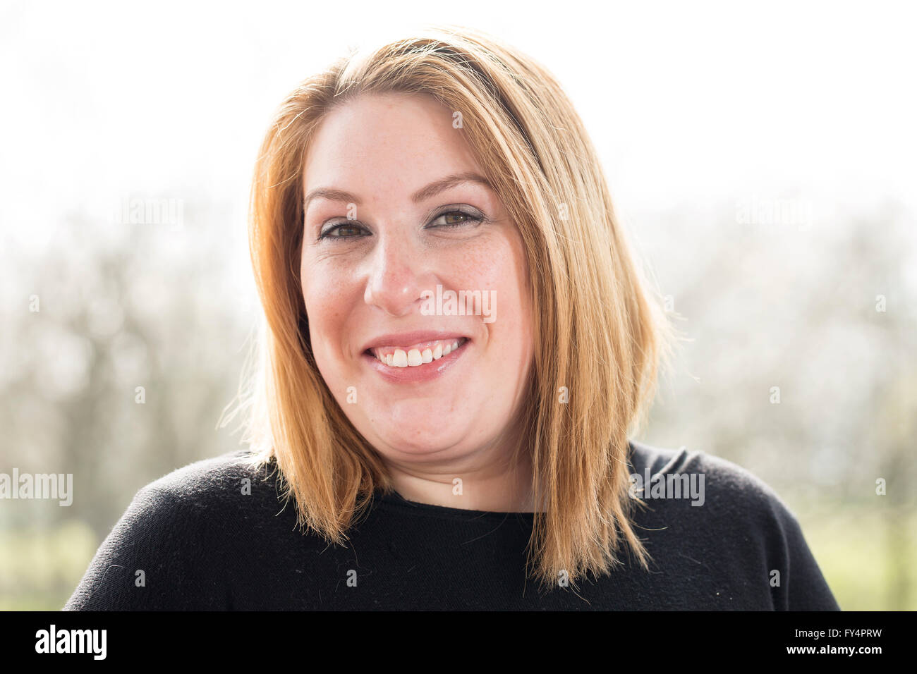 Klassische Kopfschuss. Eine junge Frau in einem schwarzen Top und kurzen blonden Haaren steht außen zurück, die von der Sonne beschienen. Sie hat ihren Kopf gekippt Stockfoto
