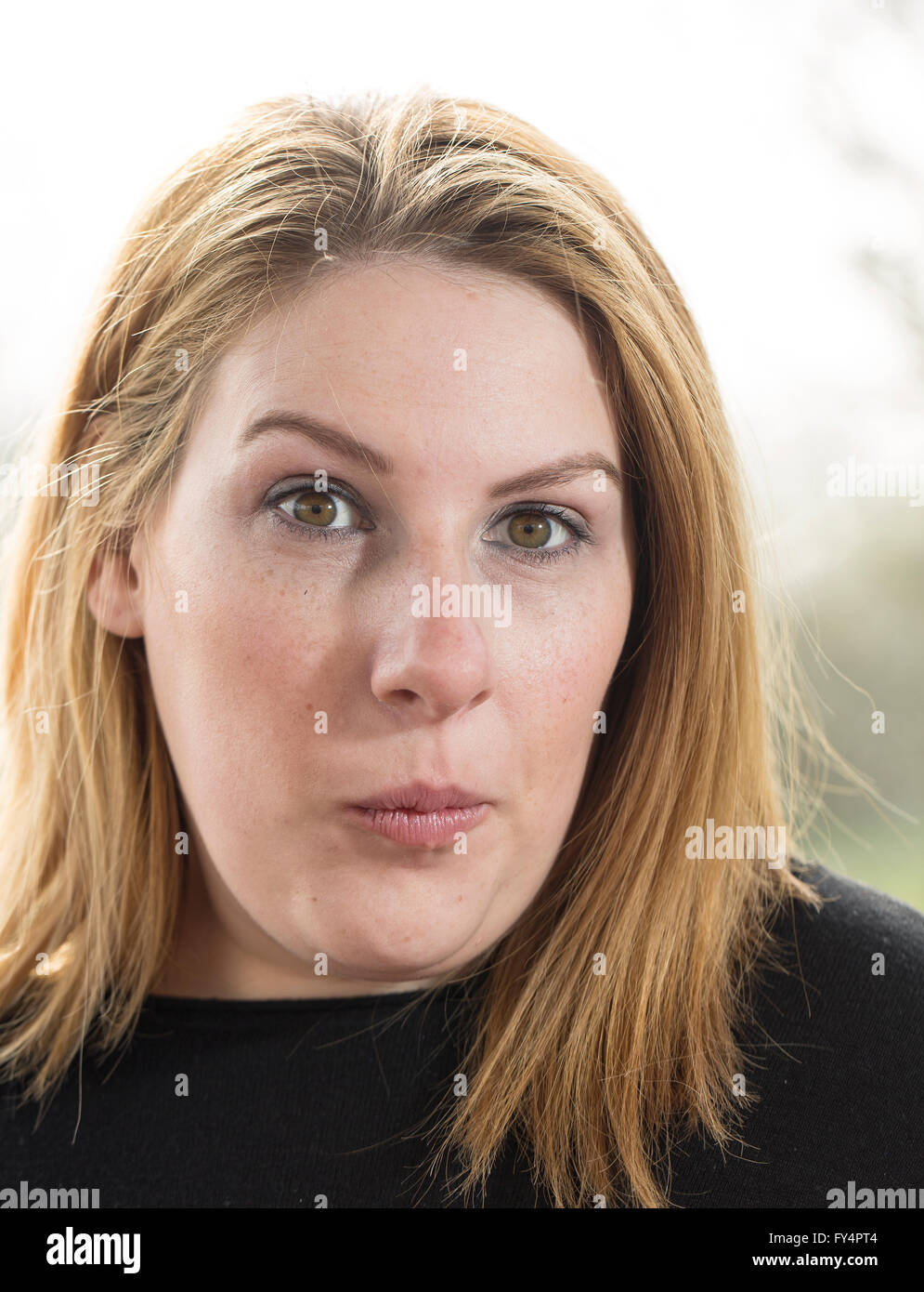 Klassische Kopfschuss. Eine junge Frau in einem schwarzen Top und kurzen blonden Haaren steht außen zurück, die von der Sonne beschienen. Sie ist überrascht und ha Stockfoto