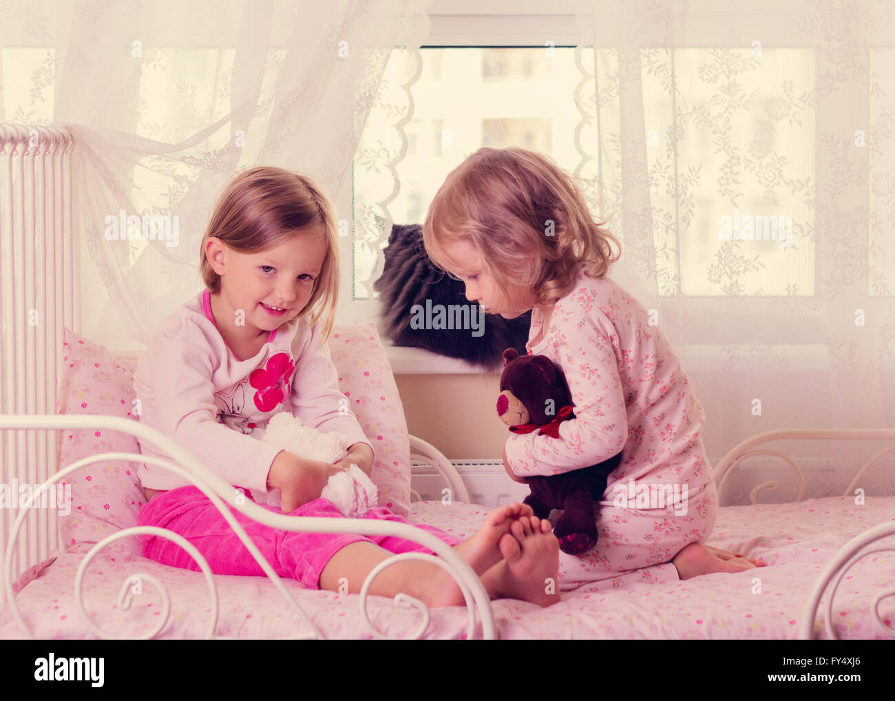 Süße lustige kleine Mädchen (Schwestern) spielen im Bett, am Fenster sitzt eine Katze. Selektiven Fokus. Stockfoto