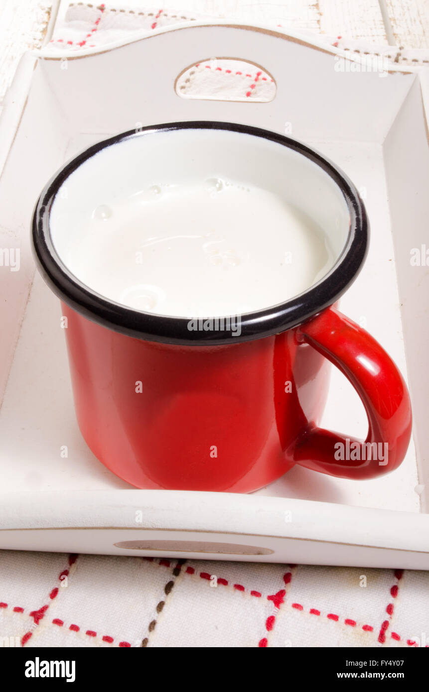 warme Milch in einem roten Emaille Becher auf Holz Serviertablett Stockfoto