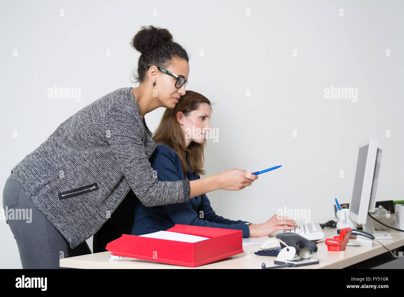 Zwei Business-Frauen vor dem Computer im Büro. Beide Frauen sind auf der Suche auf den Monitor. Eine Frau zeigt auf die m Stockfoto