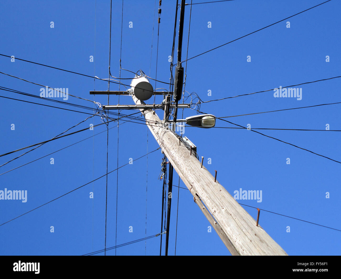 Hohen Hochspannungsleitungen schneiden sich an einem hölzernen Strommast mit Straßenlaterne in Berkeley, Kalifornien. Stockfoto