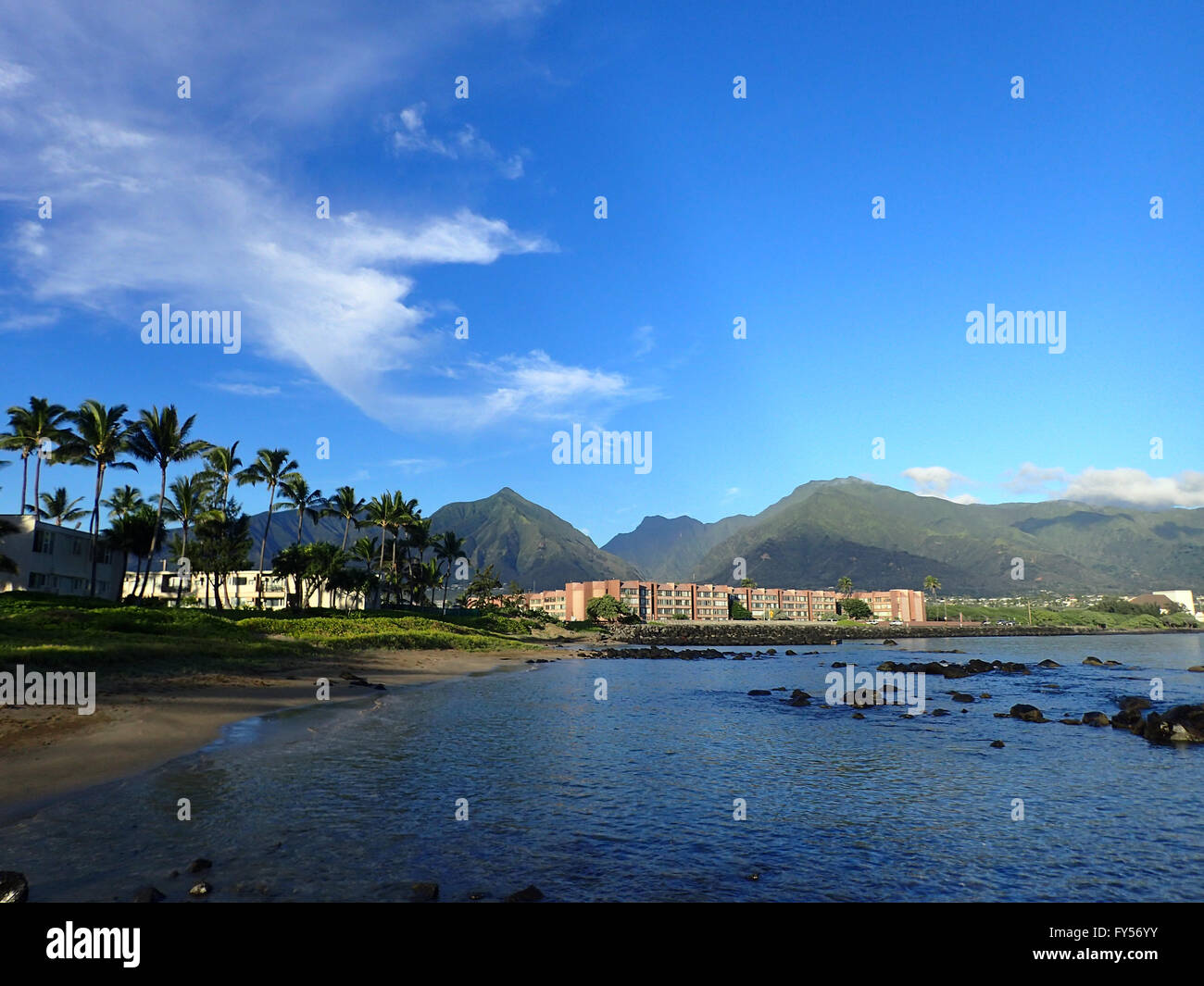 Kahului Bucht mit Hotel, Kokospalmen, und Iao Valley und die umliegenden Berge in der Ferne auf West Maui an einem schönen Tag. Stockfoto