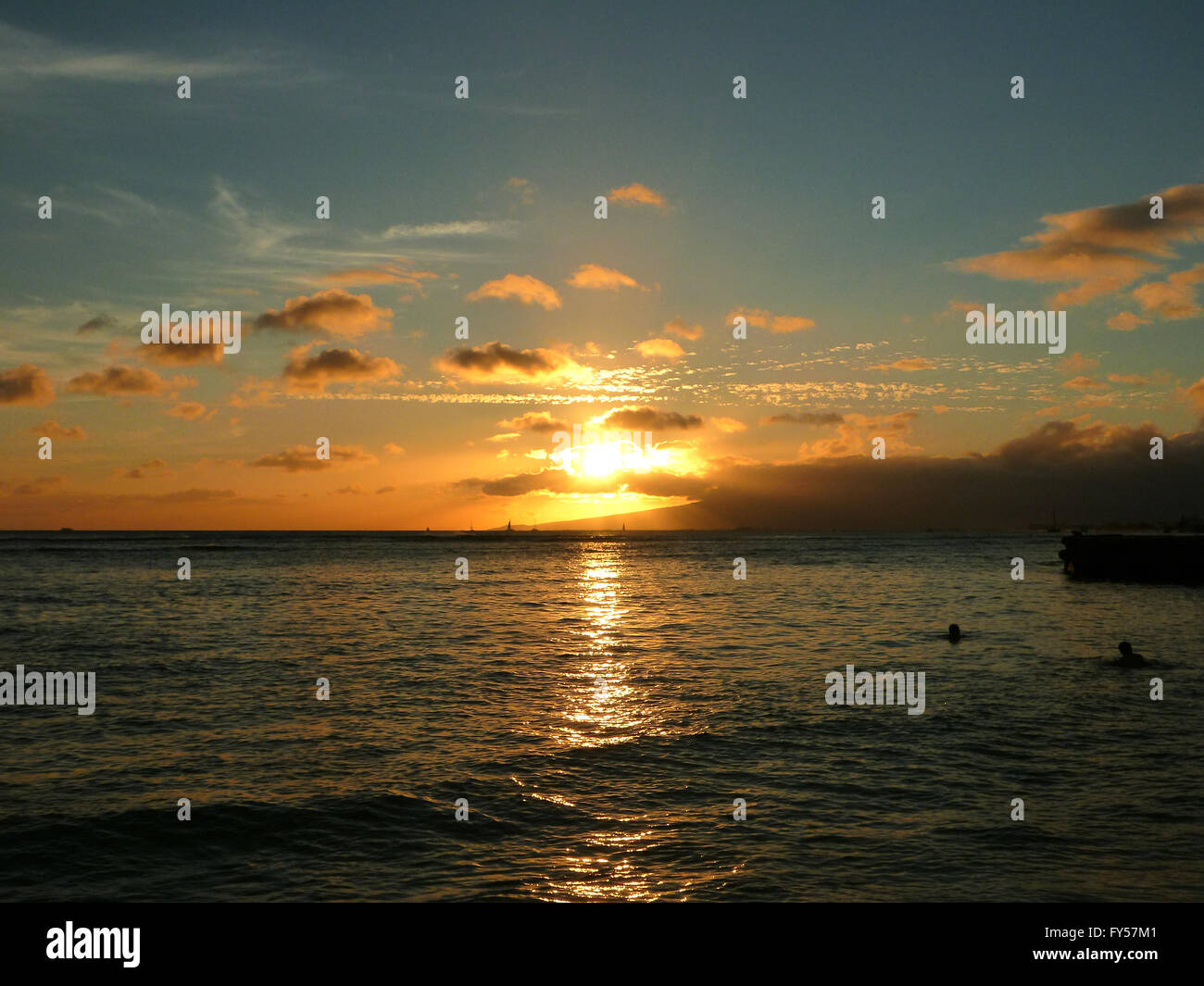 dramatischen Sonnenuntergang auf Kaimana Beach über dem Meer mit Booten Segeln auf dem Wasser auf Oahu, Hawaii. Stockfoto