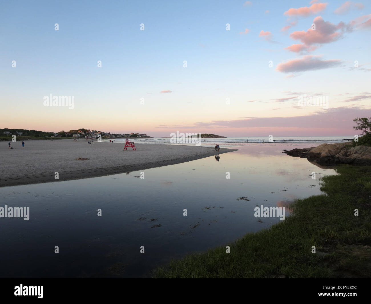 Stream mit Menschen spielen in der Brandung an Good Harbor Beach, Gloucester, Massachusetts während der Dämmerung, zum Strand führt. Mit Lifegu Stockfoto