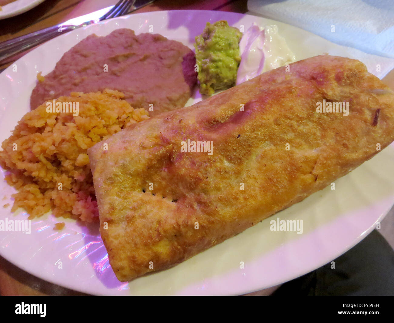 Chimichanga mit spanischen Reis, Bohnen, Seite Guacamole und Sauerrahm auf Tisch mit Serviette und Gabel, Messer. Stockfoto