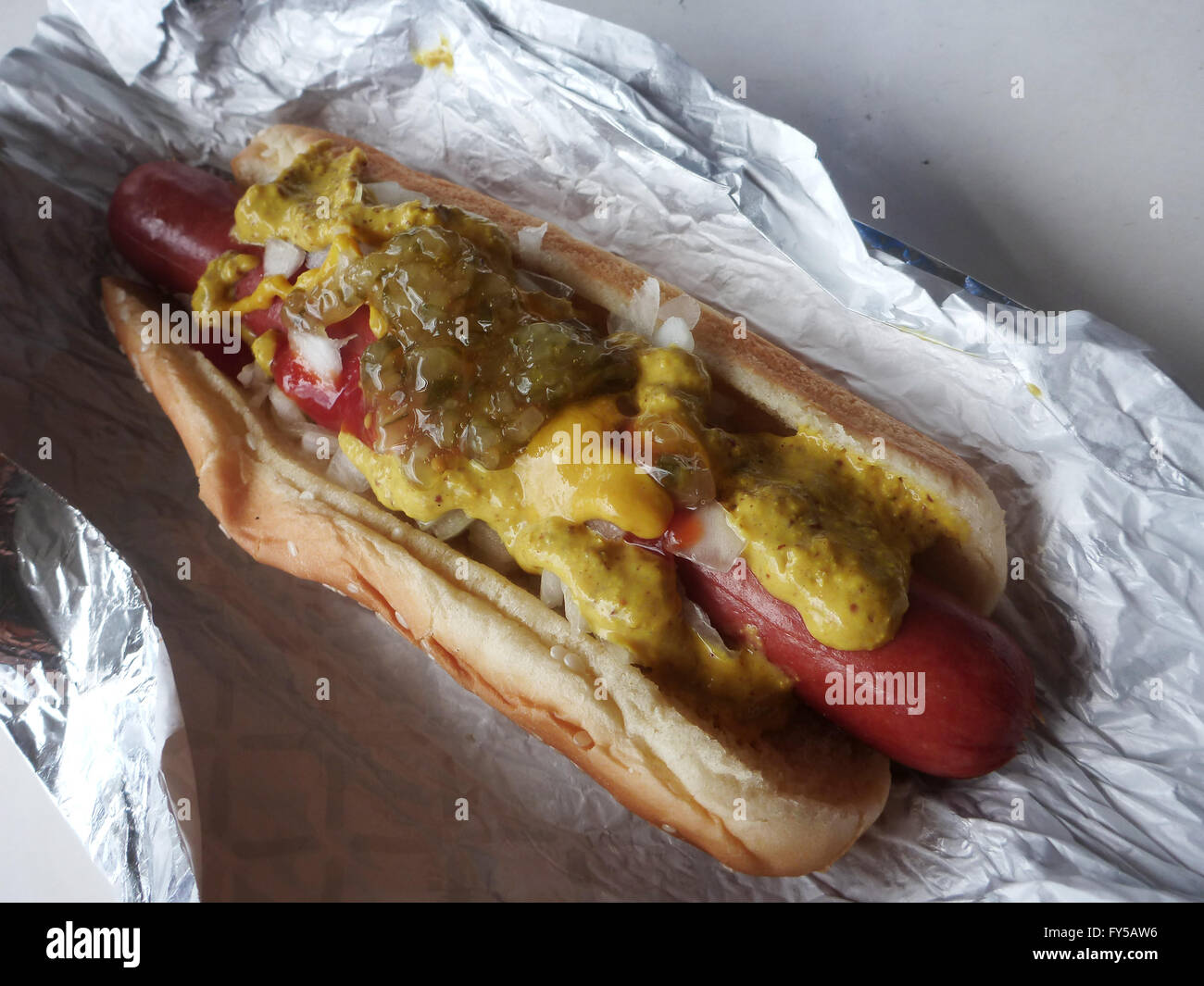 Große Hot Dog in Wrapper in Senf, Ketchup, Zwiebeln in einem Sesam-Brötchen bedeckt. Stockfoto