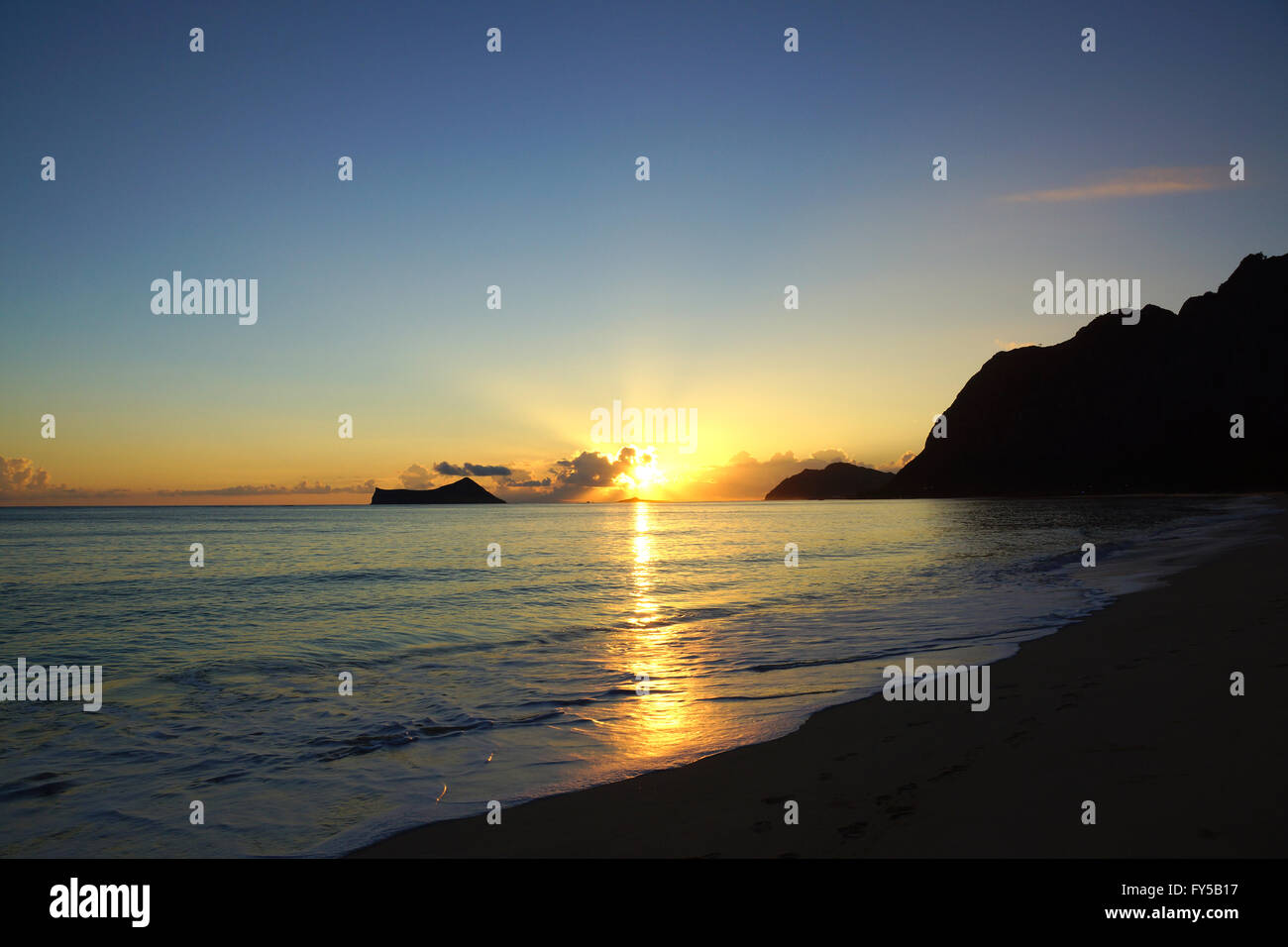 Am frühen Morgen Sonnenaufgang auf Waimanalo Beach auf Oahu, Hawaii über Felsen-Insel, die durch die Wolken platzen. Stockfoto