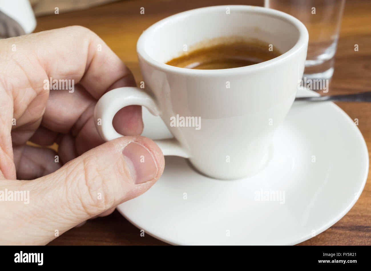 Männliche Hand, dabei kleine weiße Tasse Espresso-Kaffeemaschine Stockfoto