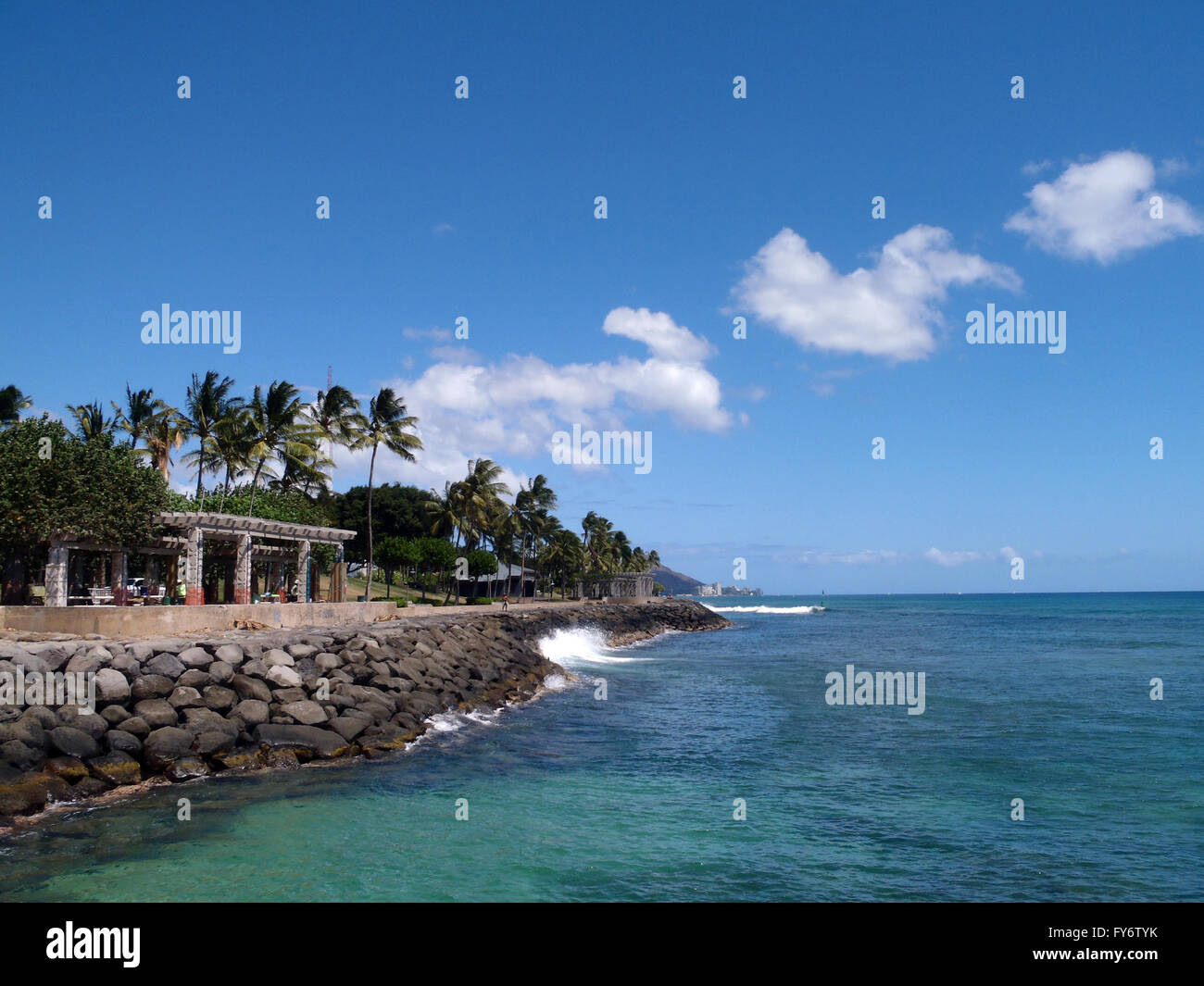 Welle stürzt gegen Felsen Ufermauer am Kaka'ako Waterfront Park mit Waikiki in der Ferne. Stockfoto