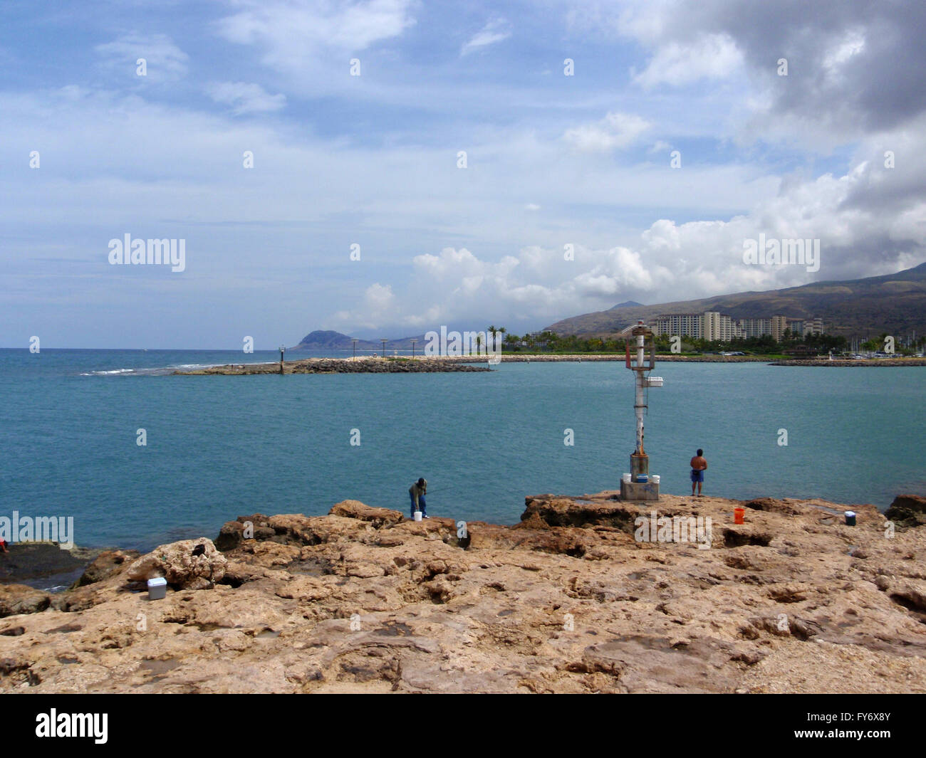zwei lokale Männer Fischen den Eingang nach Ko Olina Harbor auf Oahu mit ausgefallenen Resorts in der Ferne. Stockfoto