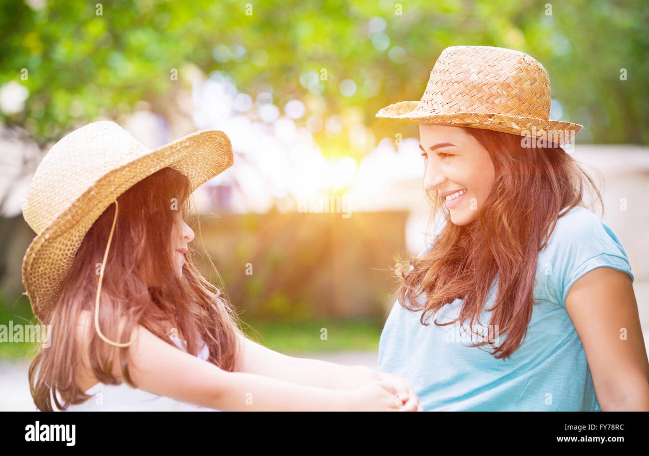 Porträt einer freudigen junge Mutter mit ihrer niedlichen fröhliche Tochter gleichen Stroh Hüte tragen und spielen im freien Stockfoto