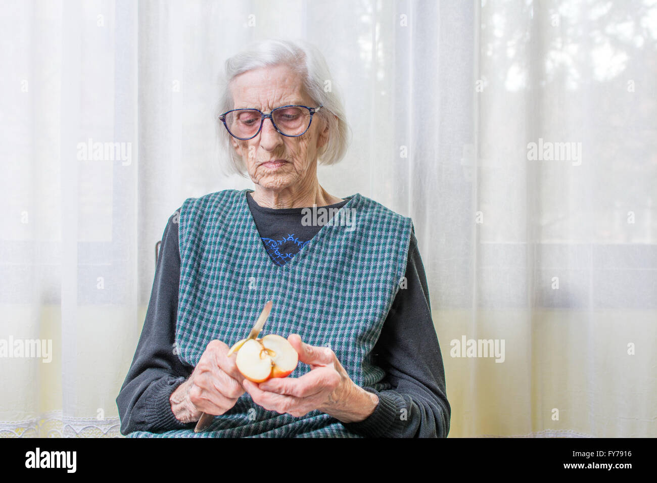 Neunzig Jahre alt Oma schneiden und schälen eines Apfels im Innenbereich Stockfoto