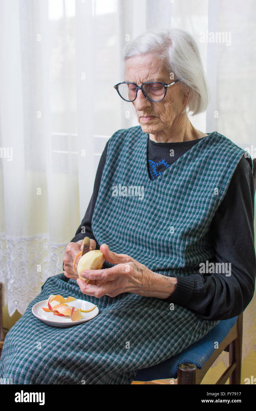 Neunzig Jahre alt Oma schneiden und schälen eines Apfels im Innenbereich Stockfoto