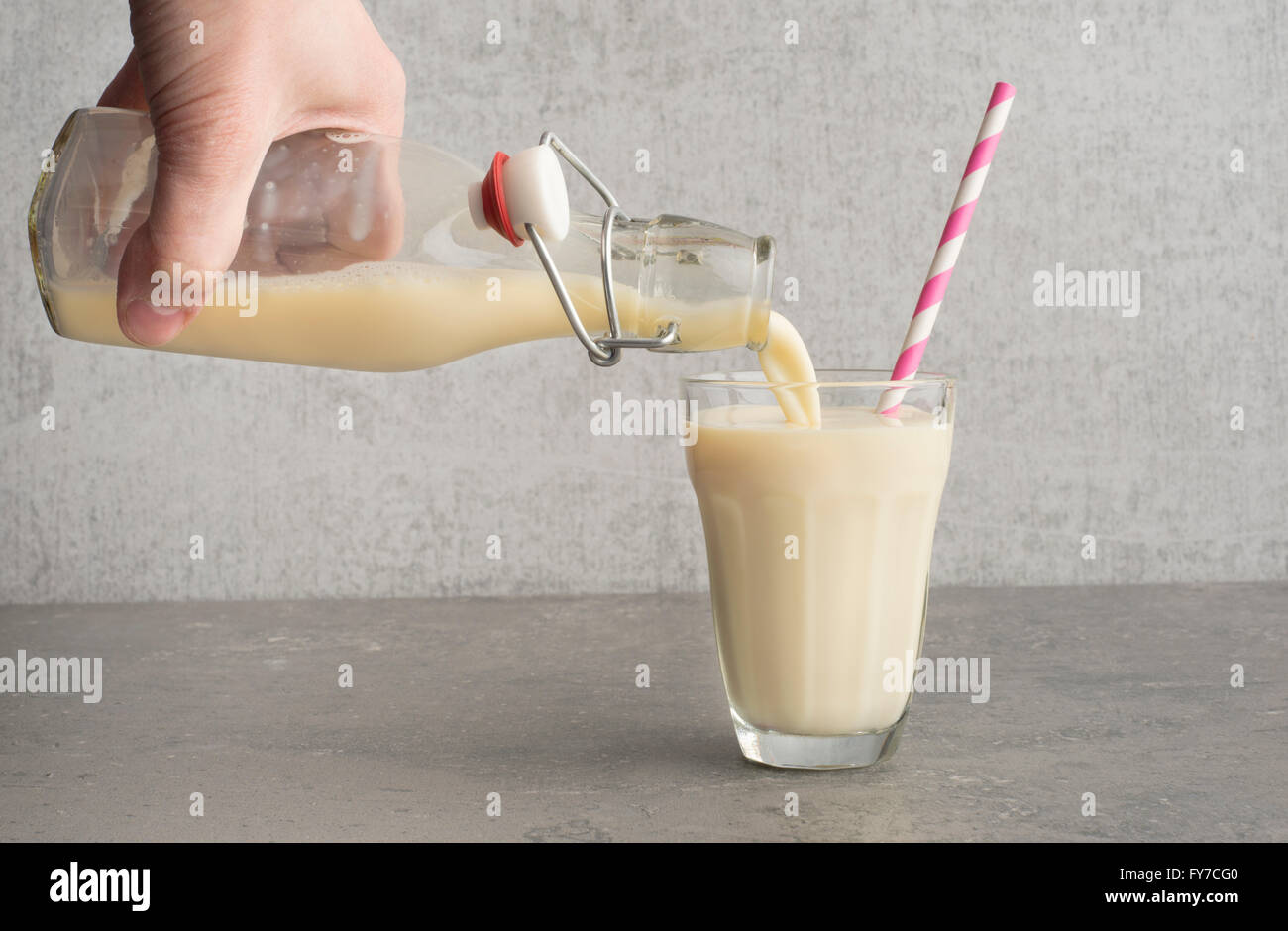 Soja-Milch aus der Flasche in ein Trinkglas mit einem gestreiften Strohhalm gegossen wird. Stockfoto
