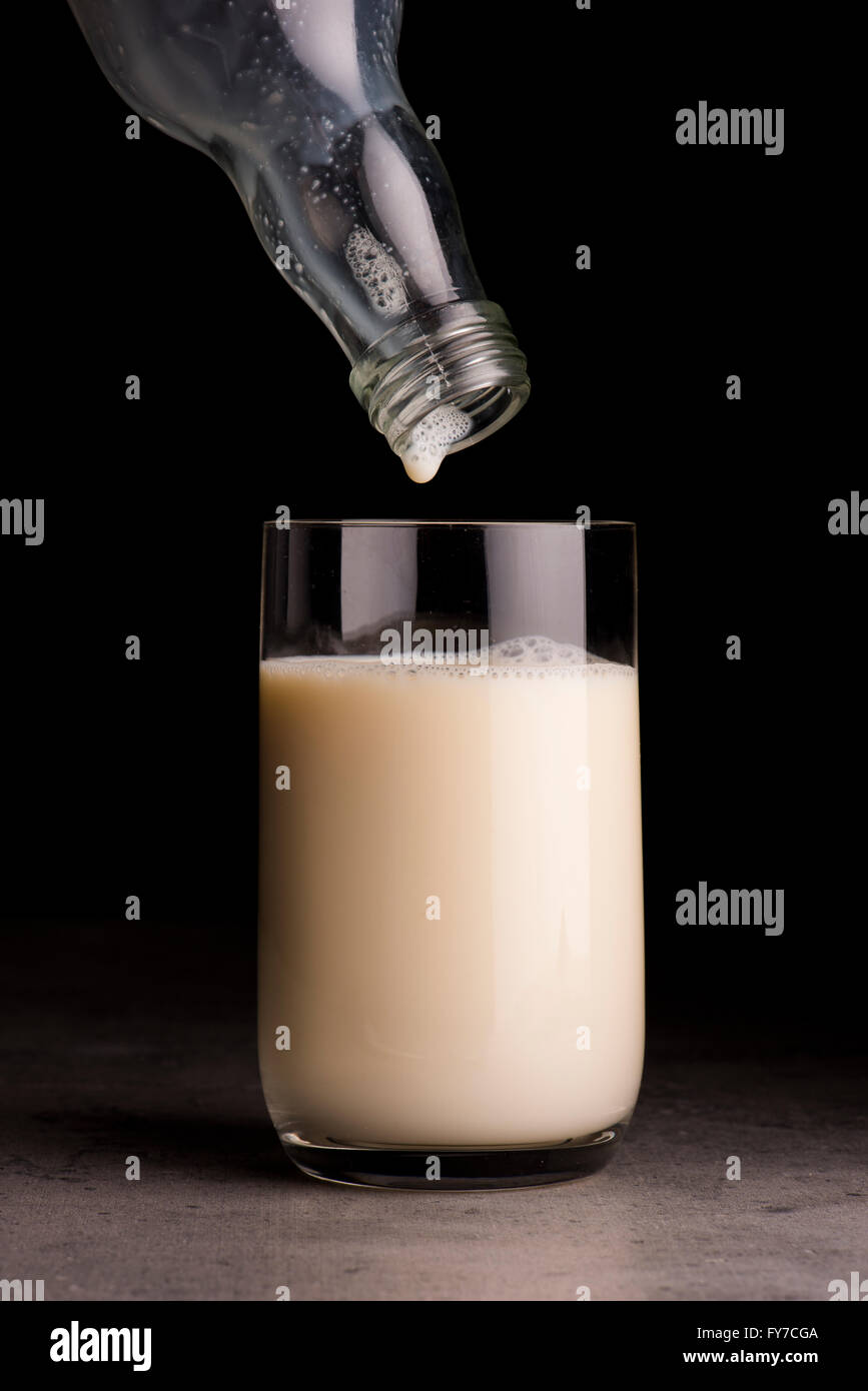 Soja-Milch aus der Flasche in ein Glas gegossen wird. Schwarzer Hintergrund. Stockfoto