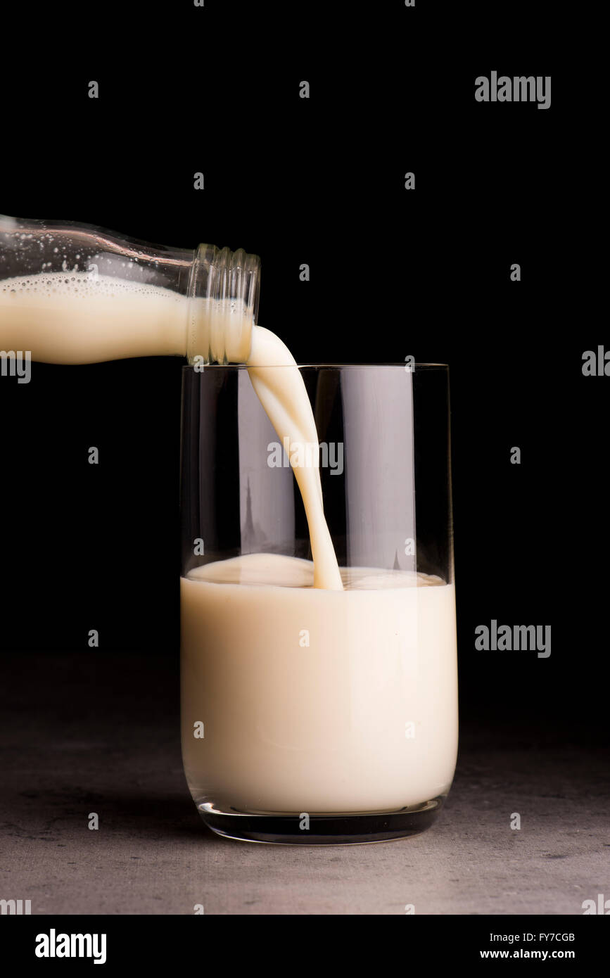 Soja-Milch aus der Flasche in ein Glas gegossen wird. Schwarzer Hintergrund. Stockfoto