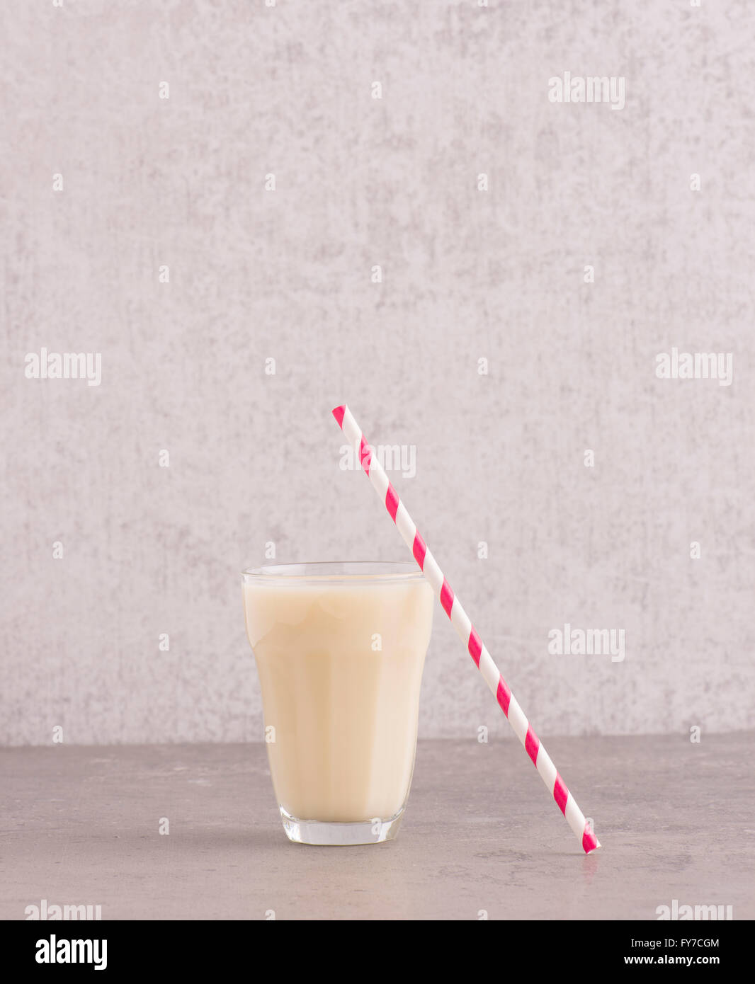 Hafermilch in ein Glas mit gestreiften trinken Stroh am Steintisch. Hintergrund mit textfreiraum Steinmauer. Stockfoto