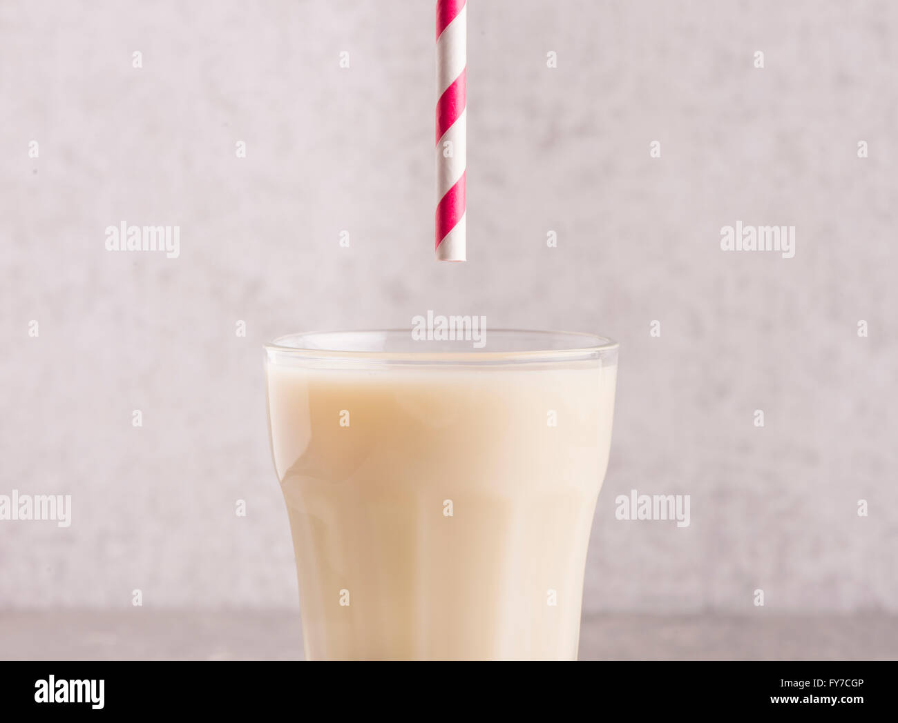 Hafermilch in ein Glas mit gestreiften Trinkhalm oben. Stein Wand Hintergrund. Stockfoto
