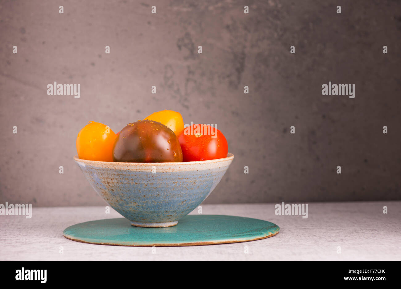 Stillleben mit Tomaten in Schüssel auf Küchentisch ist es eine Tomate mischen mit anderen Farben Stein Wand Hintergrund mit Kopie Stockfoto