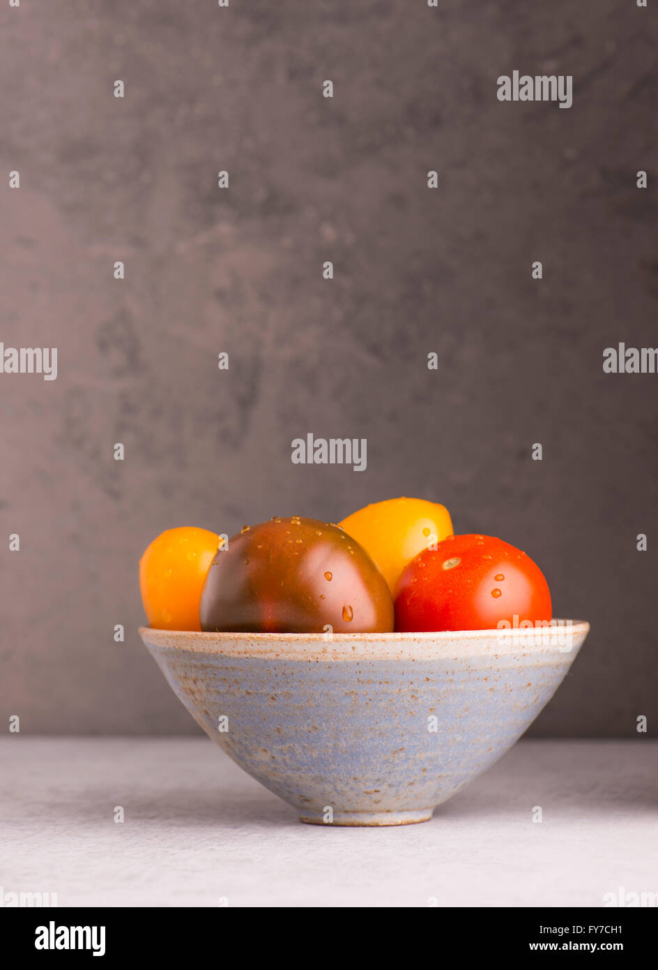 Stillleben mit Tomaten in Schüssel auf Küchentisch ist es eine Tomate mischen mit anderen Farben Stein Wand Hintergrund mit Kopie Stockfoto