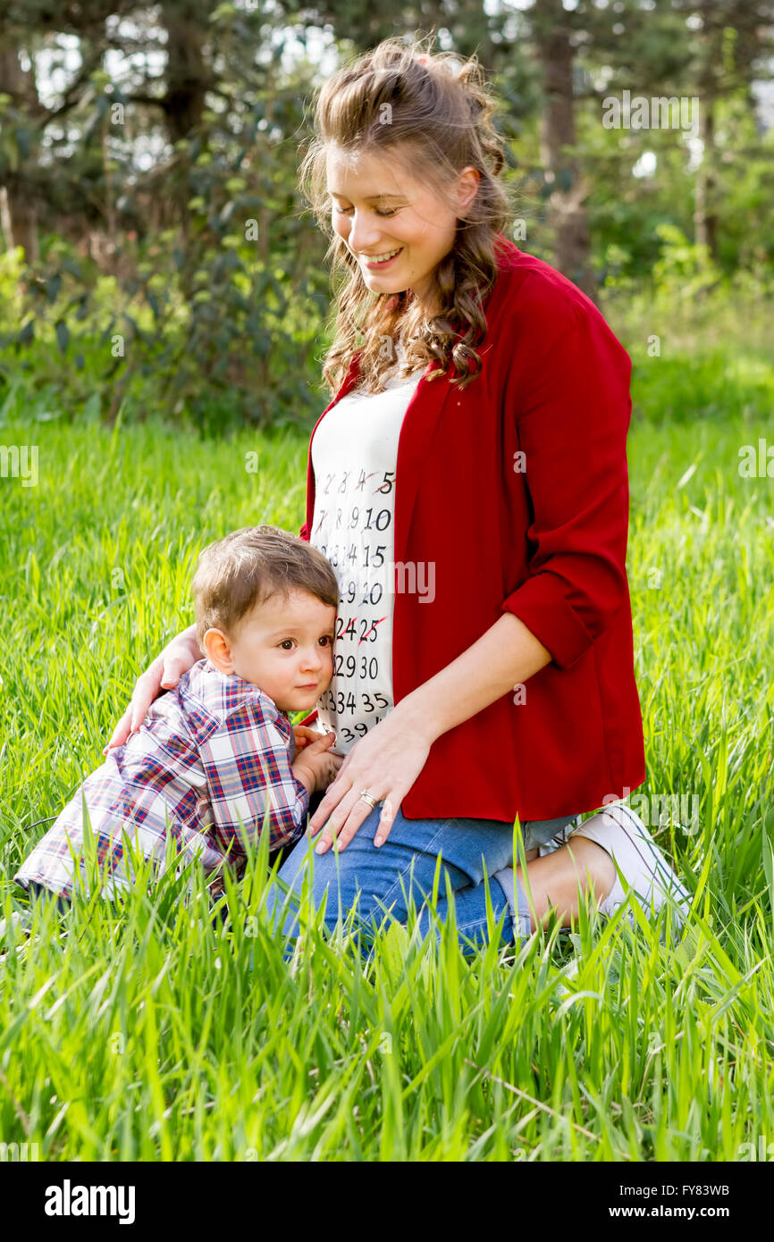 Schöne glückliche schwangere Frau mit ihrem kleinen Jungen im Park im Freien. Stockfoto