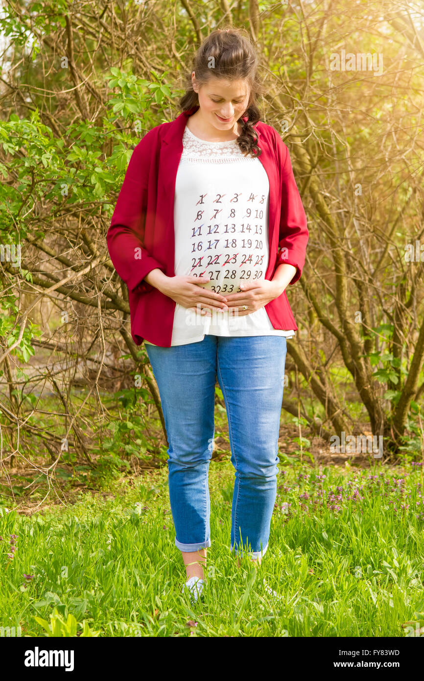 Schwangere Frau in roter Jacke mit dem Kalender auf ihr T-shirt im Freien im Park. Stockfoto