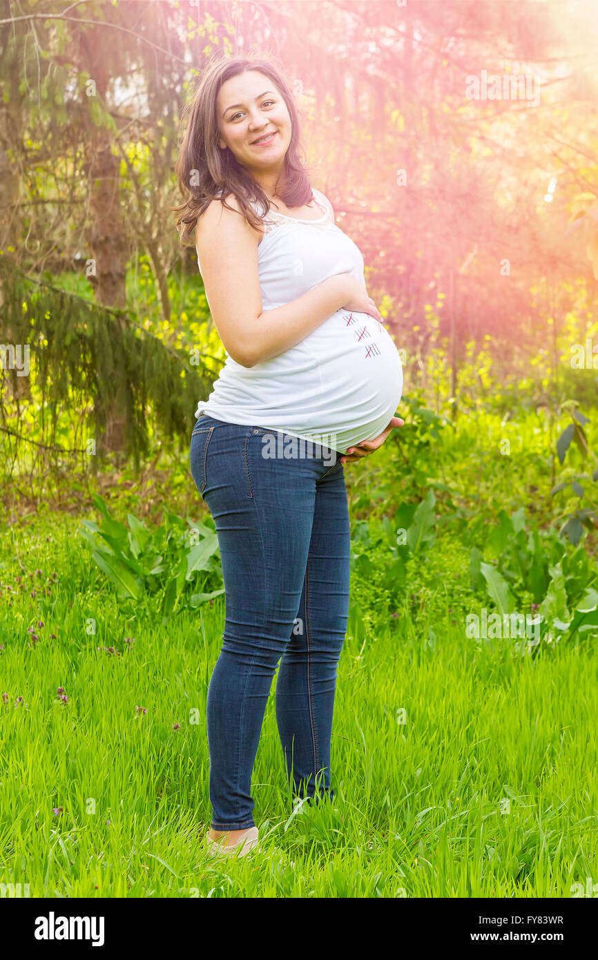 Porträt von glücklichen schwangeren jungen Frau lächelnd im Freien in warmen Sommertag. Stockfoto