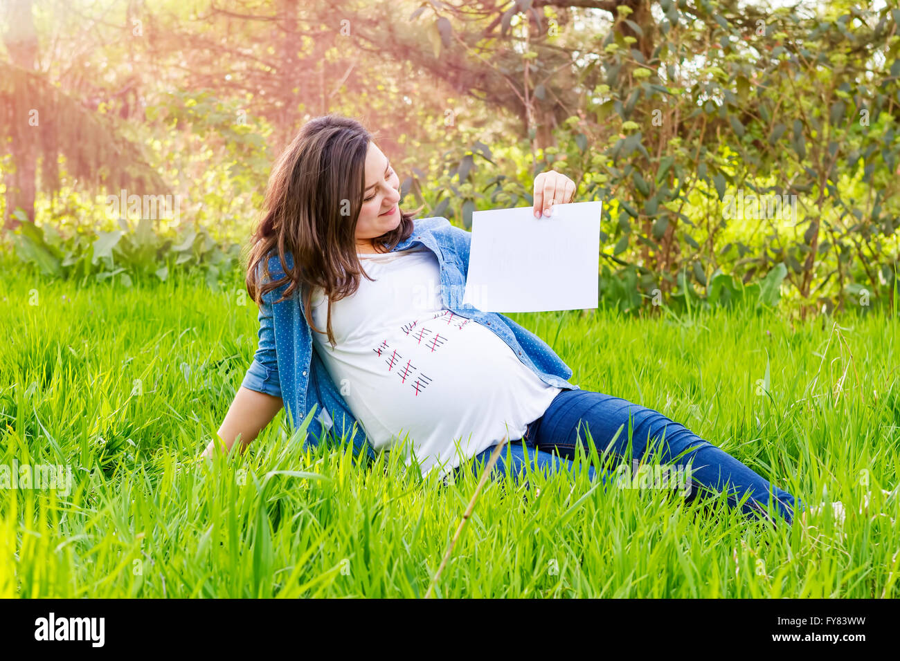 Schöne schwangere Frau im Freien mit einem Papier in der hand zeigt die Tag der Geburt ihres Babys. Stockfoto