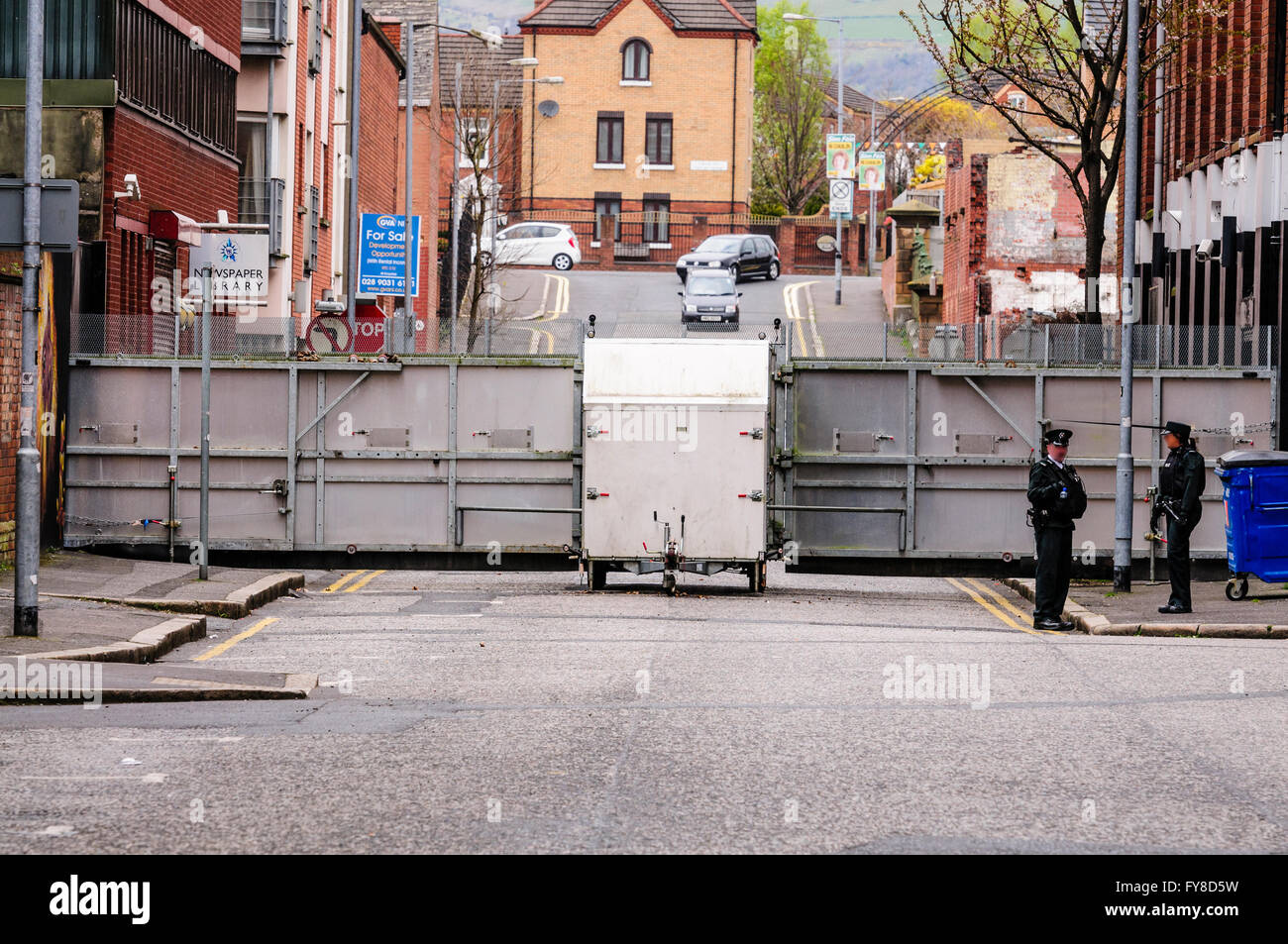 Zwei PSNI Offiziere stehen eine große Metall mobile Polizei Cordon Barriere Absperren einer Straße in Belfast während einer Parade. Stockfoto