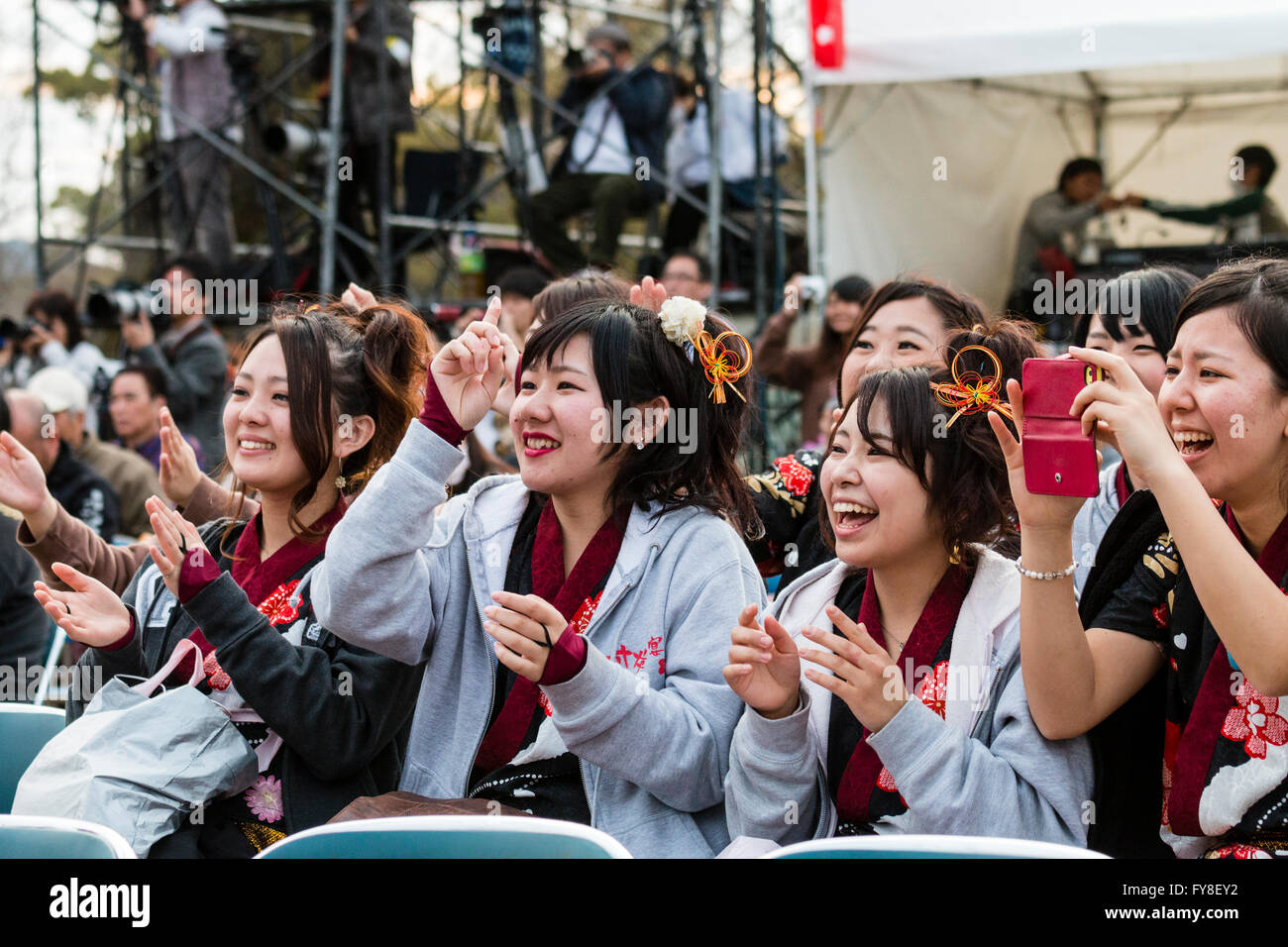 Reihe der jungen japanischen Frauen im Teenageralter, Yosakoi Tänzer, sitzt im Publikum, Lachen und Klatschen. Tagsüber. Stockfoto