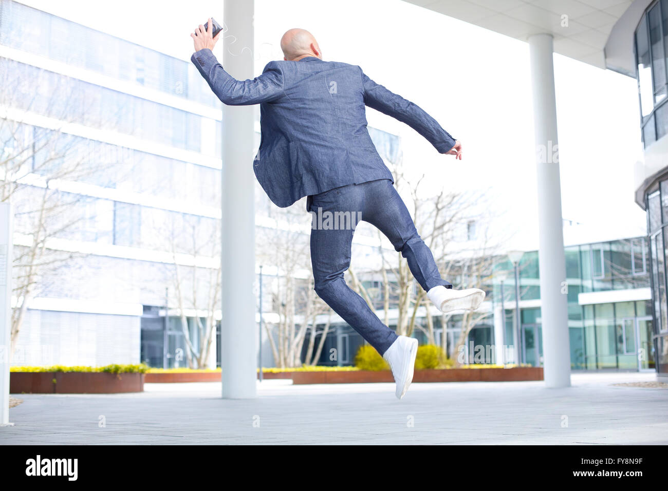 Begeisterte Unternehmer Musikhören von Smartphone und springen mitten in der Luft Stockfoto