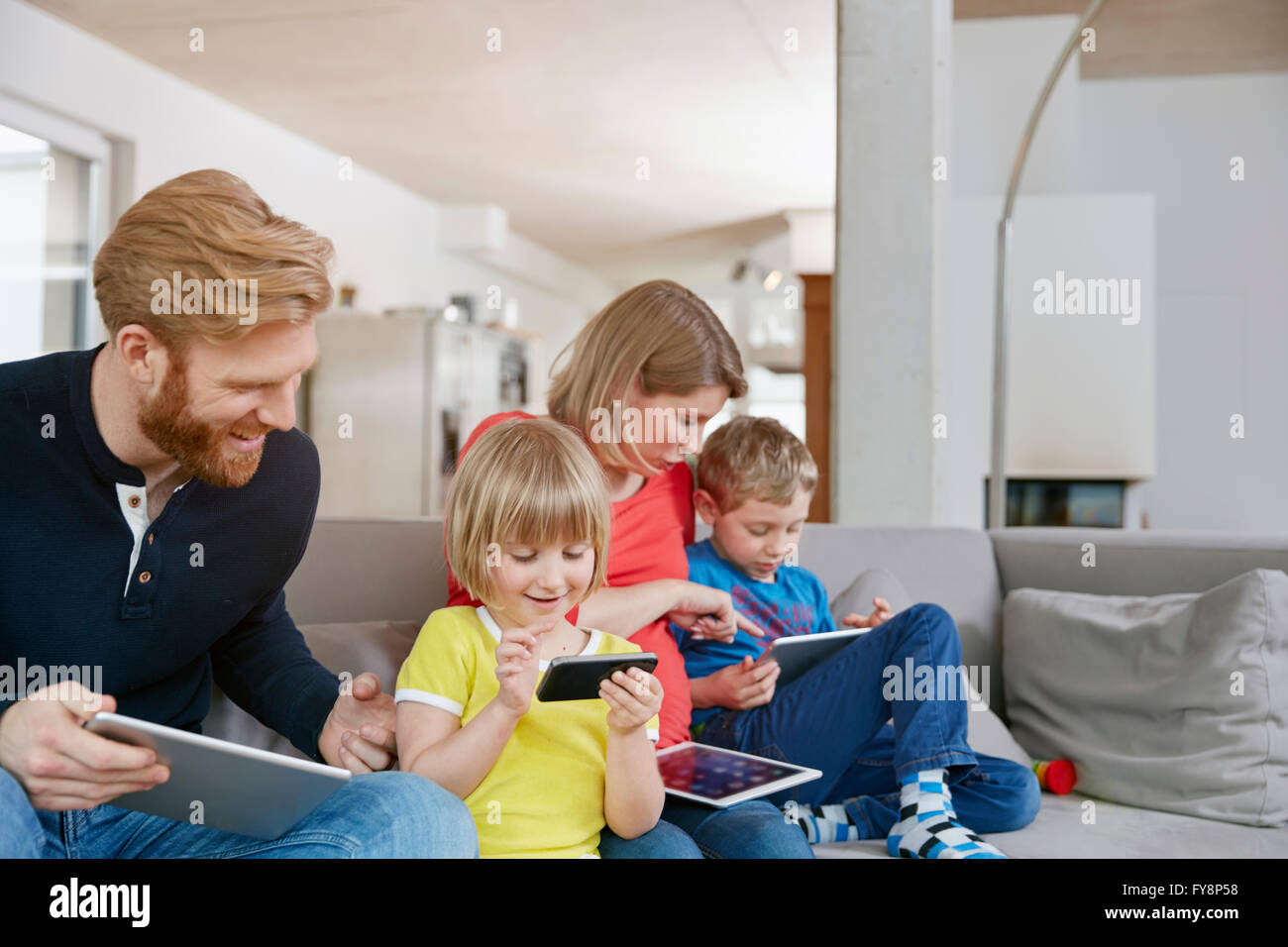 Vierköpfige Familie mit mobilen Geräten auf couch Stockfoto