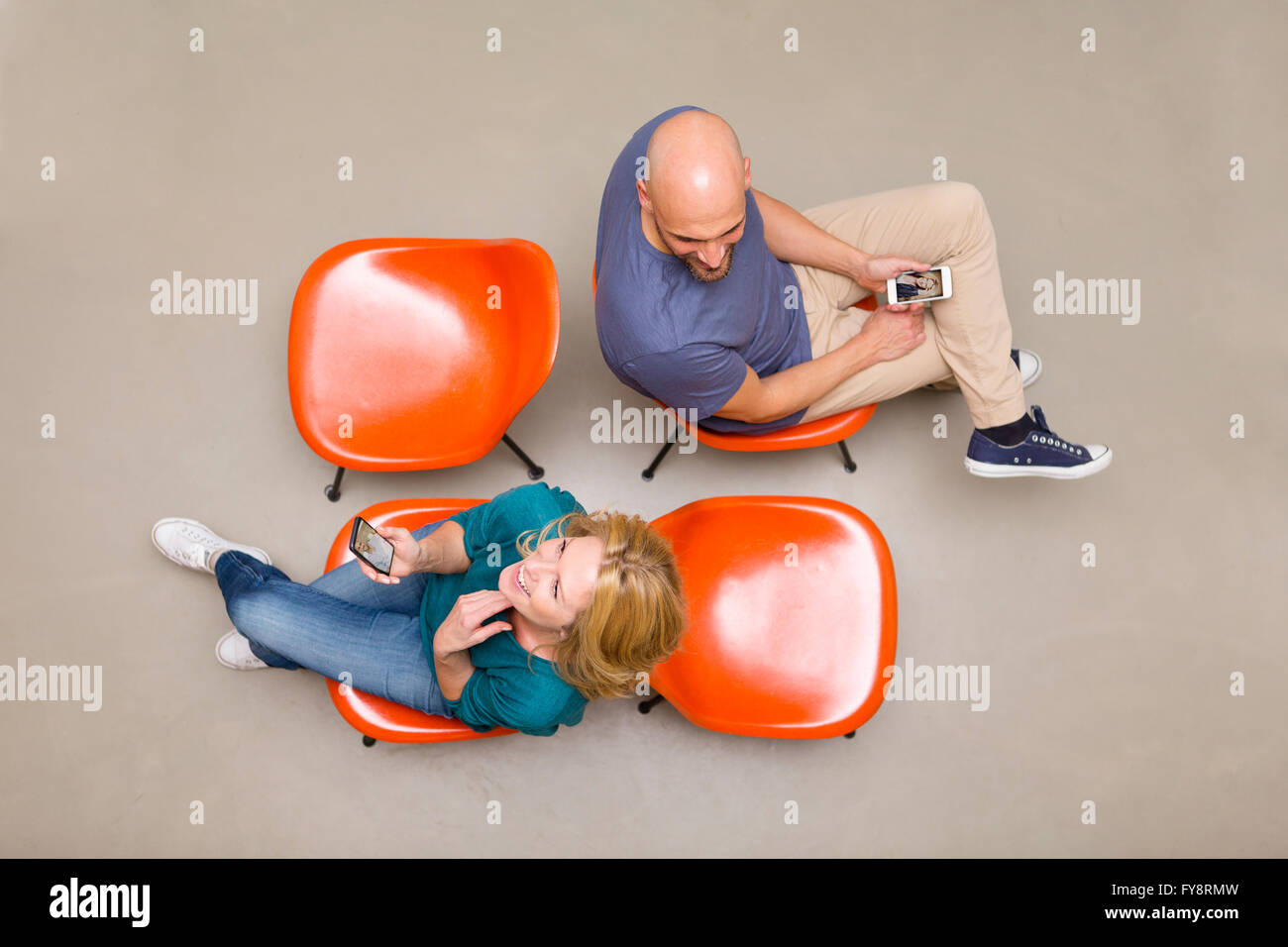 Mann und Frau sitzen auf Stühlen mit Smartphones Stockfoto