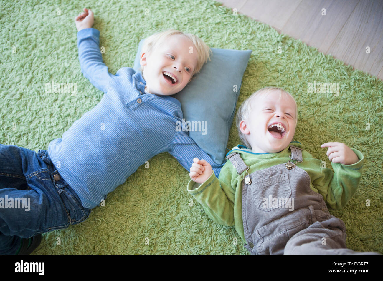 zwei kleine Brüder am grünen Teppich zu Hause liegen lachen Stockfoto