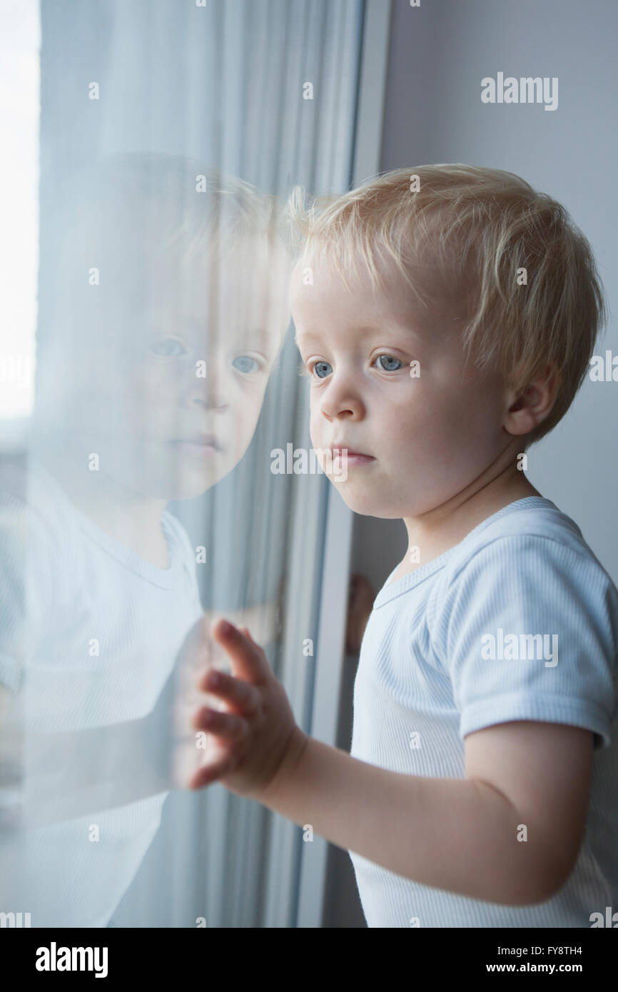 Porträt der kleinen blonden Jungen Blick durch Fenster Stockfoto