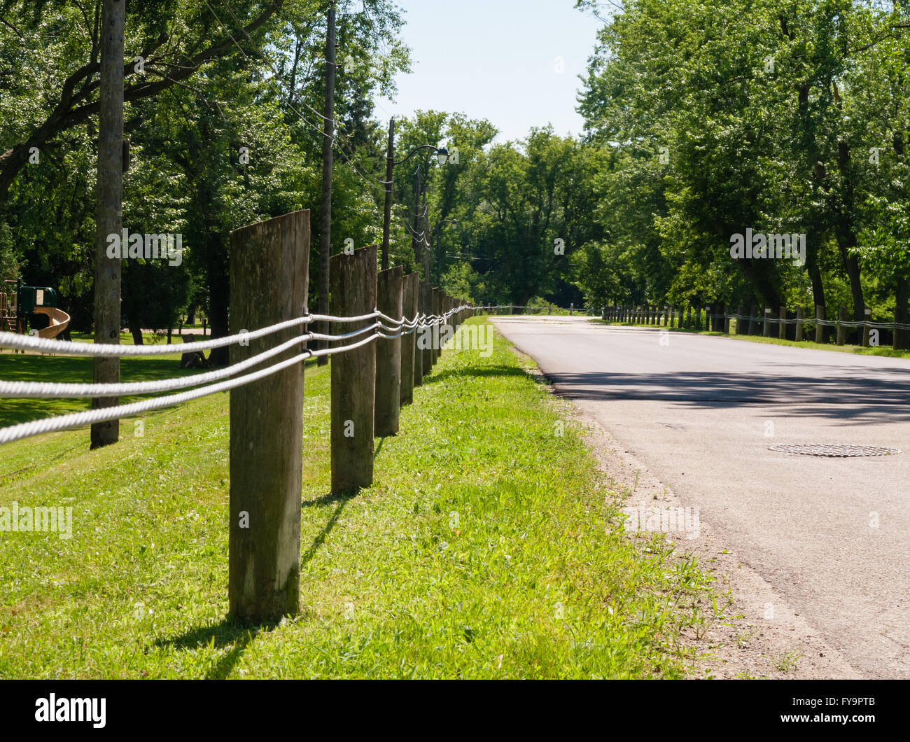 Kurze Holzzaun Beiträge mit drei parallele Linien entlang leere Straße in ländlicher Umgebung im Sommer, umgeben von Bäumen. Stockfoto