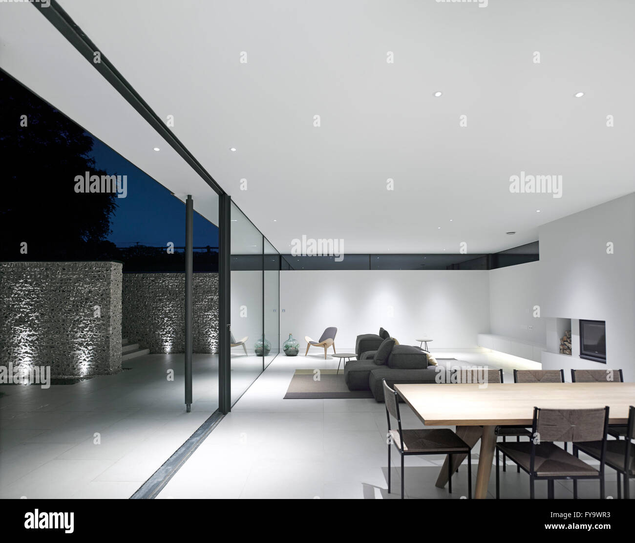 Verglaste Schiebetür zwischen Wohn-/ Esszimmer und Innenhof in der Nacht. Cheeran Haus, Lower Basildon, Großbritannien. Architekt: John Pardey Architekten, 2015. Stockfoto