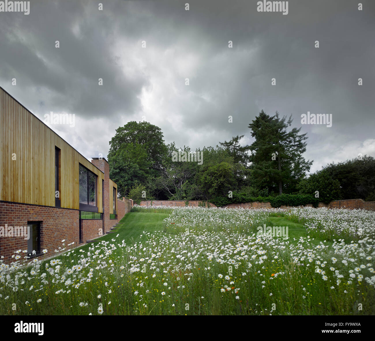 Perspektive entlang der Außenfassade inmitten einer historischen ummauerten Garten mit einer Wildblumenwiese. Cheeran Haus, Lower Basildon, Großbritannien. Architekt: John Pardey Architekten, 2015. Stockfoto