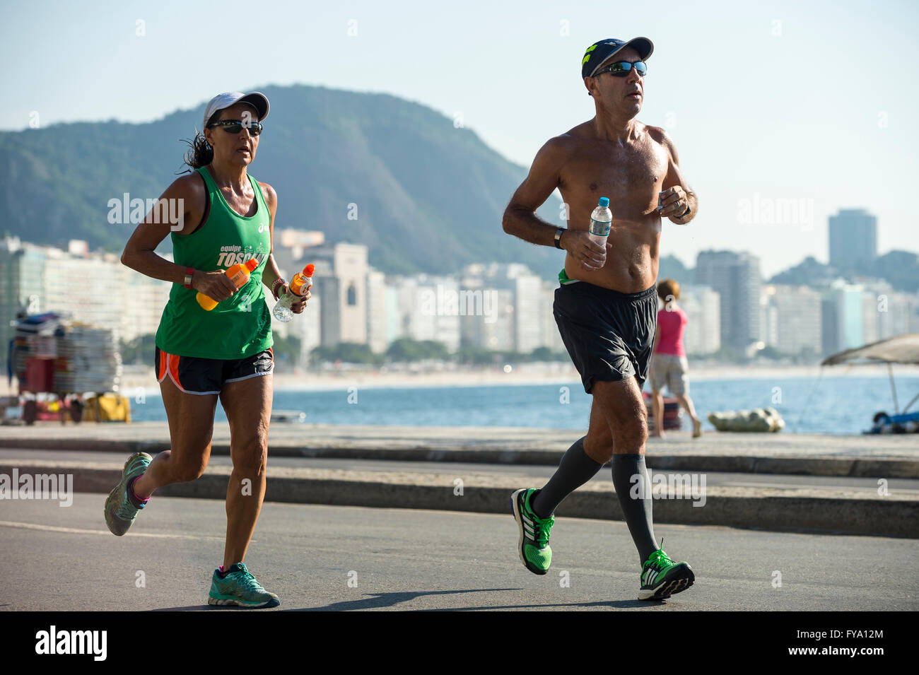 RIO DE JANEIRO - 3. April 2016: Ein paar Jogger auf die auf dem Strand Straßenpass vor der Skyline der Stadt Copacabana Stockfoto