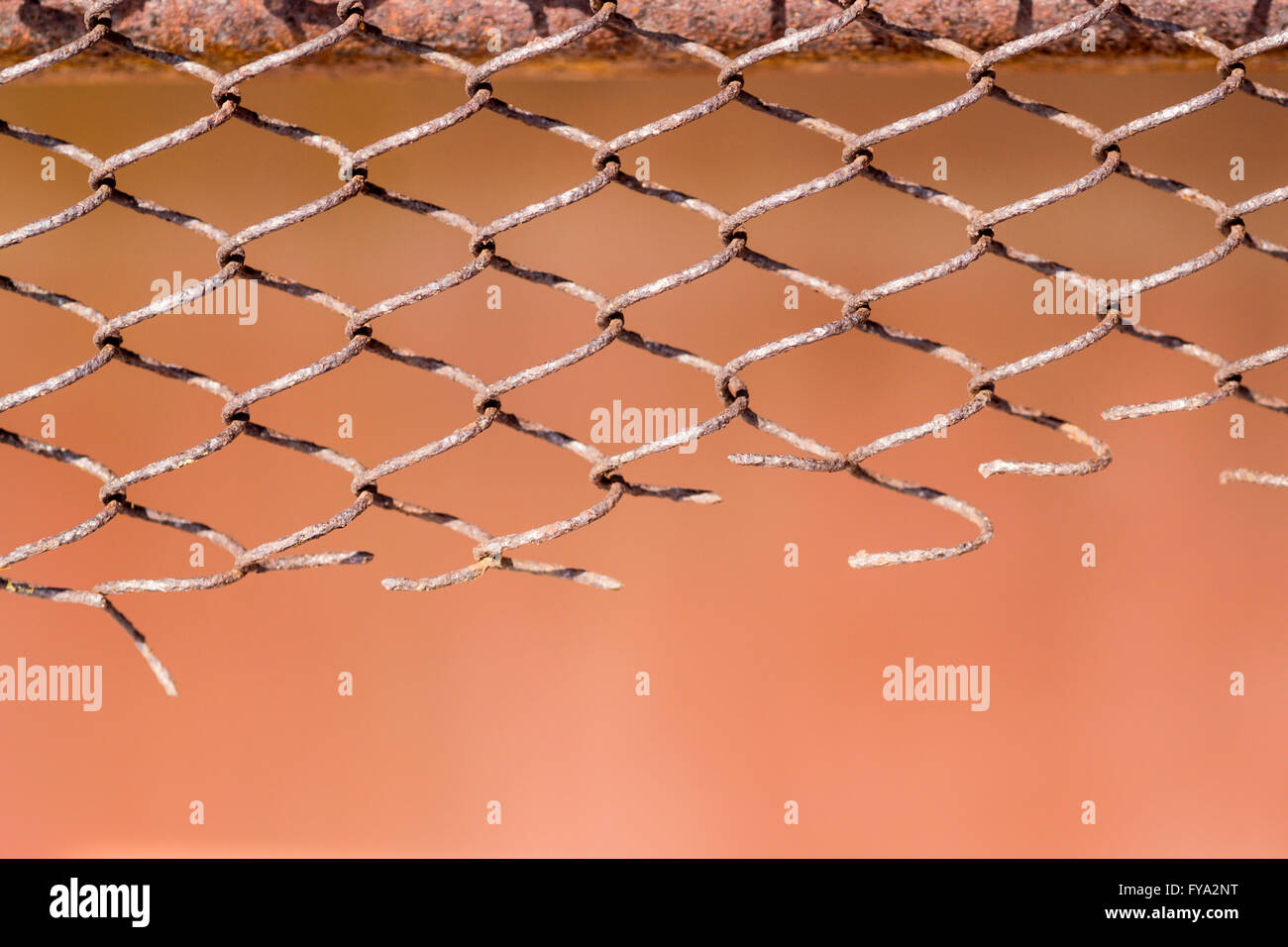 Defekte und beschädigte Maschendrahtzaun mit orangem Hintergrund Stockfoto