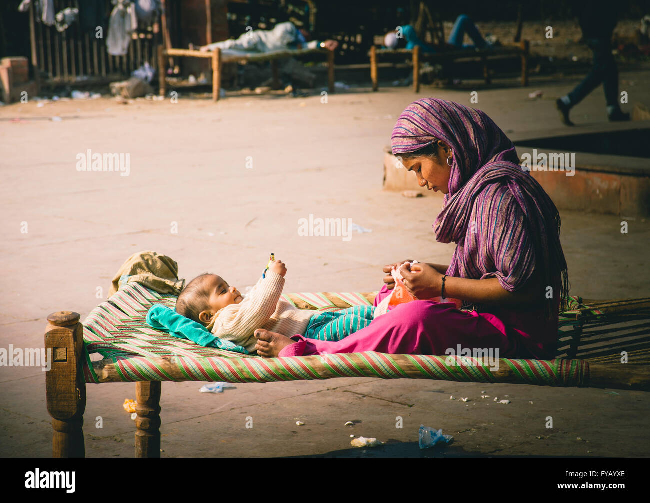 Eine junge Mutter sitzt mit ihrem Baby auf ein Charpoy außerhalb ein Elendsviertel in Old Delhi Stockfoto