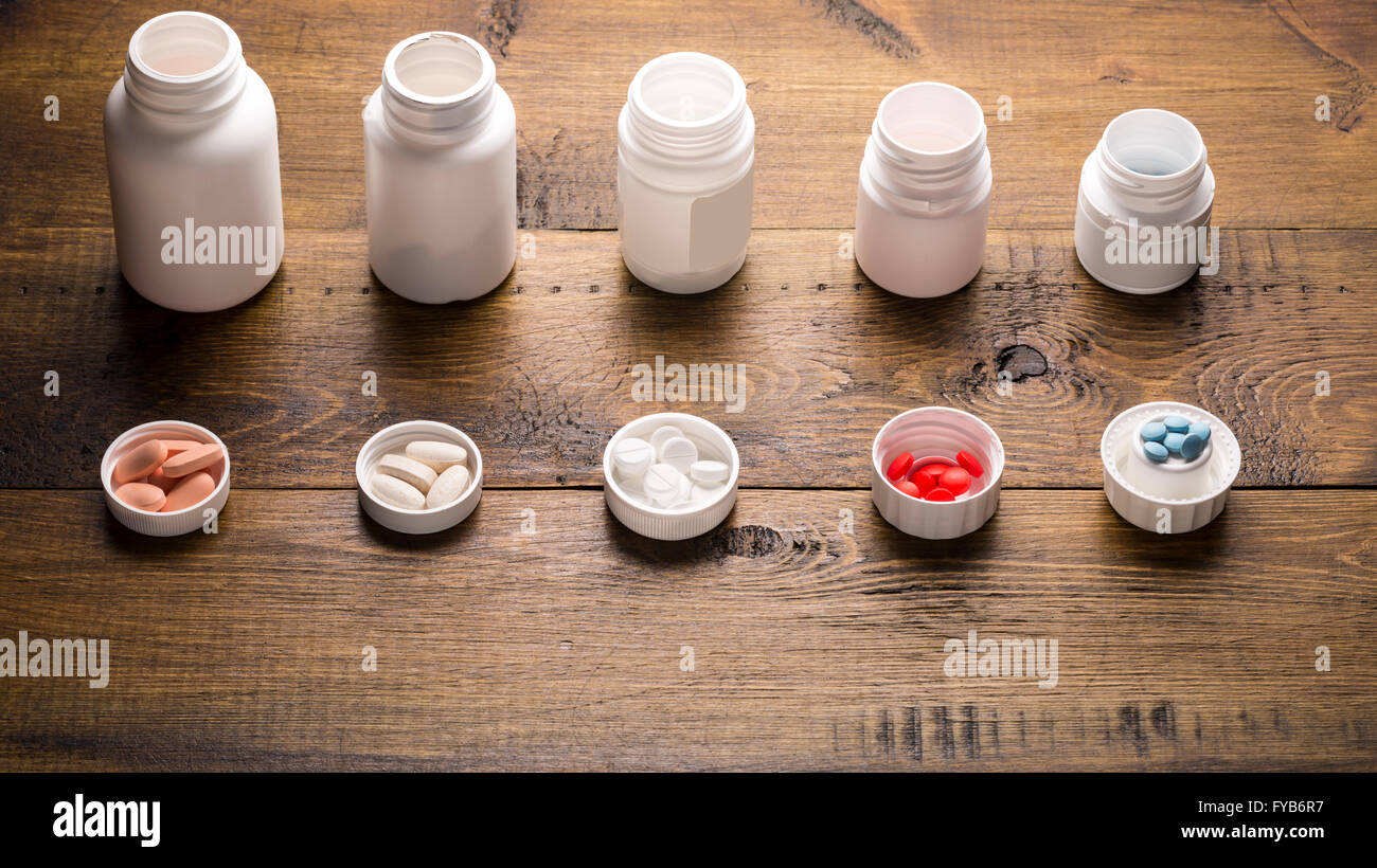 Linie der medizinischen Flaschen mit verschiedenen farbigen Pillen auf dunklem Holz Stockfoto