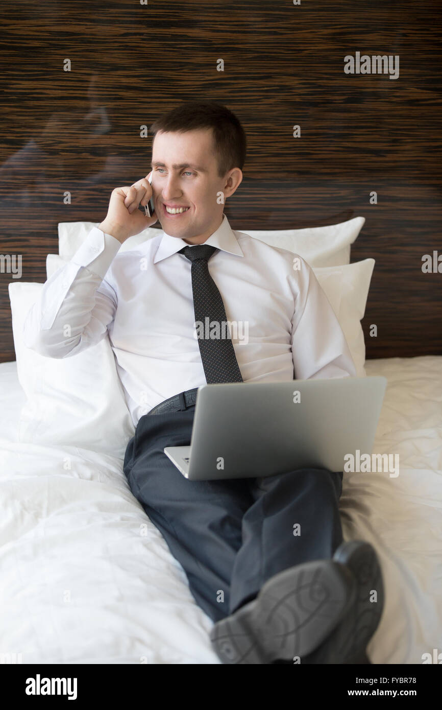 Schöne fröhliche junge Geschäftsmann mit Laptop sitzen und telefonieren. Geschäftsmann, arbeiten von zu Hause oder in Reise Stockfoto