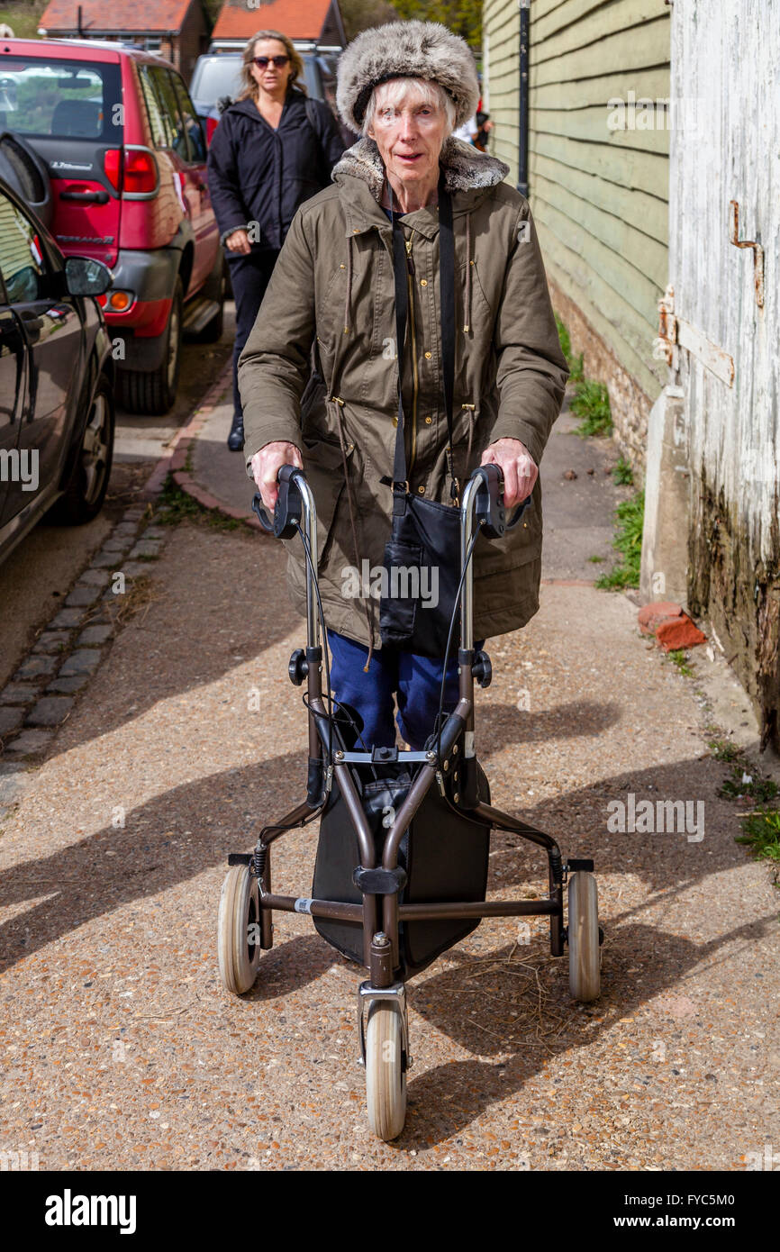 Eine weibliche Verwandte Uhren eine behinderte ältere Frau mit einem drei Rad Rollator, Sussex, UK Stockfoto