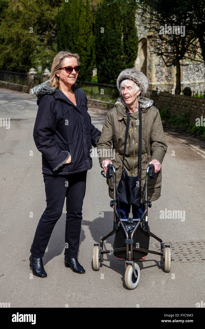 Einen weiblichen Verwandten zu Fuß mit einer behinderten älteren Frau mit einer drei-Rad Rollator, Sussex, UK Stockfoto