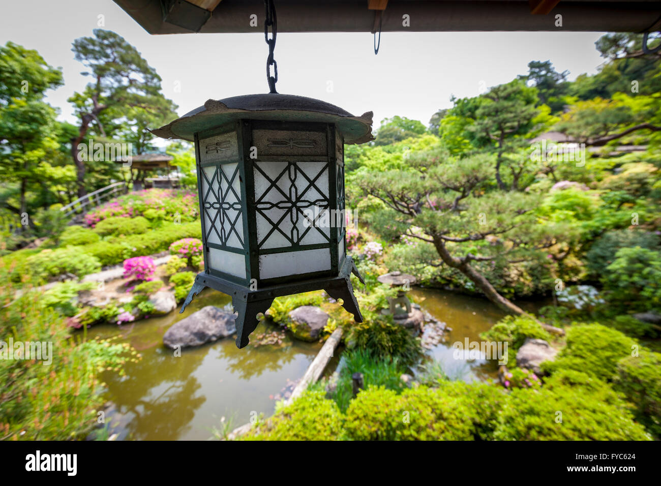 Eine traditionelle Metall Laterne hängen von einer Veranda mit Blick auf einen schönen japanischen Garten Stockfoto
