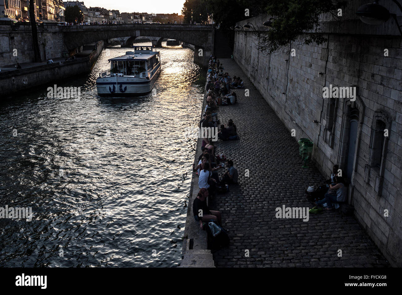 Mitglieder der Öffentlichkeit genießen den Sonnenuntergang neben einem Kanal, wenn ein Boot fahren Sie unter der Brücke in Paris. Frankreich. PIC Pako Mera Stockfoto